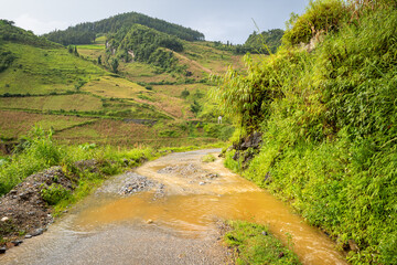 A monsoon degraded road among mountains and green forests, Asia, Vietnam, Tonkin, Bac Ha, towards Lao Cai, in summer on a sunny day.