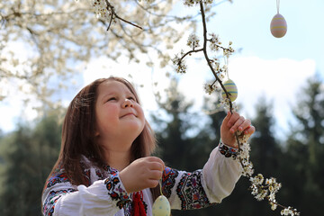 Pretty ukrainian girl wearing vyshyvanka decorating the tree with easter eggs. happy family...