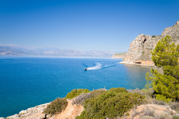 The arid rocky coast and its green countryside along small beaches, in Europe, Greece, Peloponnese, Argolis, Nafplio, Myrto seashore, in summer, on a sunny day.