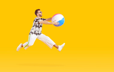 Funny young man tourist wearing casual clothes with inflatable beach ball going on summer holiday trip isolated on studio yellow background and jumping. Vacation, journey and travel concept.