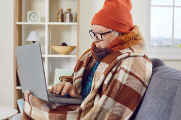 Elderly man working at home with laptop and trying to warm up with heating problems. Retired man in...