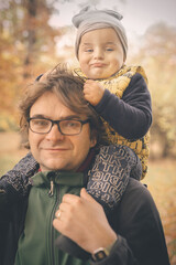 Man carrying his son on the shoulders in late fall park