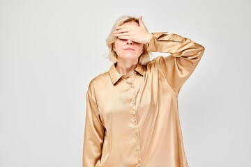 Portrait of young blonde woman covering eyes with hand isolated on white studio background.