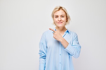 Young blond woman in casual pointing aside finger, demonstrating empty space for product or text...