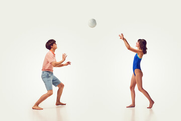 Young people, man and woman, friends playing beach volleyball, having fun on seaside resort against white background. Concept of summer vacation, travelling, retro style, fashion, leisure