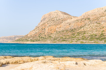 The sandy beach with pink reflections at the foot of the rocky cliffs, in Europe, Greece, Crete, Balos, By the Mediterranean Sea, in summer, on a sunny day.