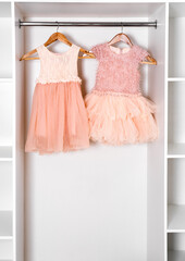 Elegant peach color dresses hanging on wooden racks in white wardrobe.