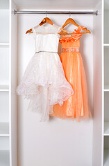 White and orange puffy dresses hang on hangers in modern white dressing room.
