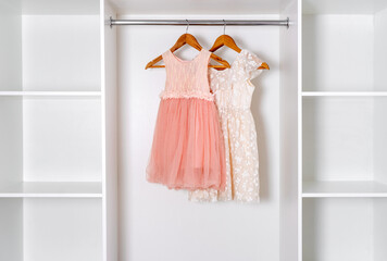 White and coral puffy dresses hang on hangers in modern white dressing room.