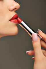 cropped view of glamorous young woman applying red lipstick on grey background, beauty and makeup