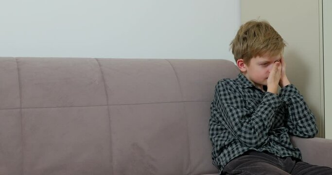 Boy is suffering from toothache sitting on the sofa at home