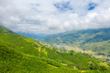 Naklejka na ściany i meble The traditional village on the mountainsides with tropical forests with green and yellow rice terraces, in Asia, Vietnam, Tonkin, Sapa, towards Lao Cai, in summer, on a cloudy day.