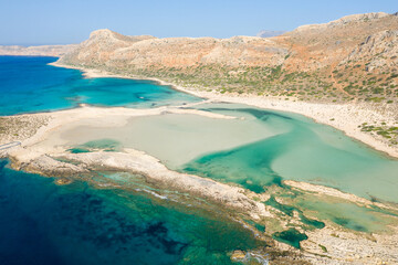 The sandy beach with pink reflections at the foot of the rocky cliffs, in Europe, Greece, Crete, Balos, By the Mediterranean Sea, in summer, on a sunny day.