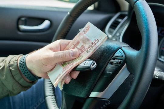 A man holding Russian rubles banknotes in his hand while driving a car. The concept of buying a car.