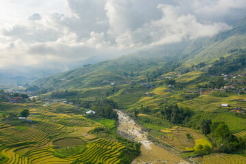 The traditional village with green and yellow rice fields in the green mountains, Asia, Vietnam, Tonkin, Sapa, towards Lao Cai, in summer, on a cloudy day.