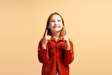 Smiling attractive little girl wearing stylish casual clothes pointing fingers up, looking up