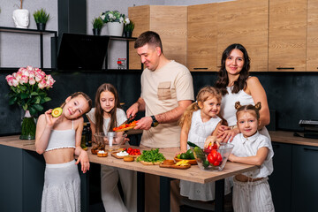 Large family - mom, dad and four daughters together prepare salad for lunch in modern kitchen. Big family together concept.