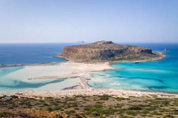 The sandy beach with pink reflections at the foot of the rocky cliffs, in Europe, Greece, Crete, Balos, By the Mediterranean Sea, in summer, on a sunny day.