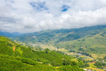 Fototapeta na wymiar The traditional village on the mountainsides with tropical forests with green and yellow rice terraces, in Asia, Vietnam, Tonkin, Sapa, towards Lao Cai, in summer, on a cloudy day.