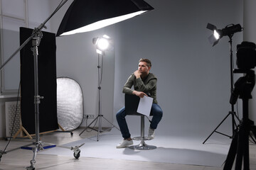 Casting call. Man with script sitting on chair against grey background in studio