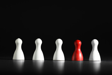 Choice concept. Red pawn among white ones on black table