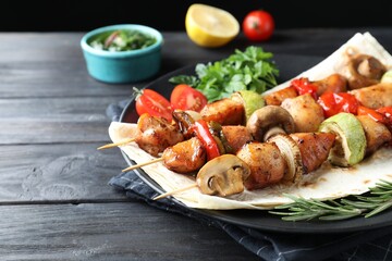 Delicious shish kebabs with vegetables served on black wooden table, closeup