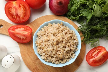 Delicious pearl barley in bowl served on white table, flat lay