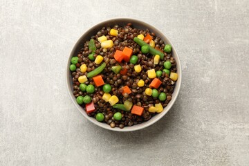 Delicious lentils with vegetables in bowl on light grey table, top view