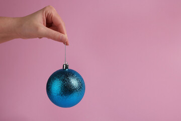 Woman holding blue Christmas ball on pink background, closeup. Space for text