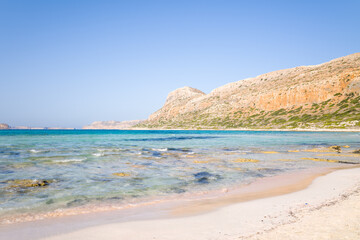 Fototapeta na wymiar The sandy beach with pink reflections at the foot of the rocky cliffs, in Europe, Greece, Crete, Balos, By the Mediterranean Sea, in summer, on a sunny day.