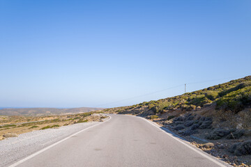 An asphalt road in the middle of the countryside and mountains , in Europe, Greece, Crete, towards Sitia, By the Mediterranean Sea, in summer, on a sunny day.
