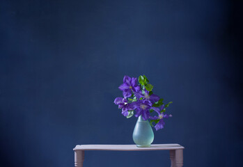 clematis flowers in glass vase  on vintage wooden shelf