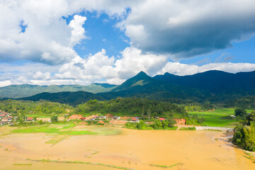 A traditional village by a lake and flooded rice fields in the middle of the mountains, Asia, Vietnam, Tonkin, Dien Bien Phu, in summer, on a sunny day.