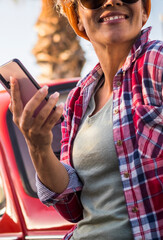 People with phone and car travel lifestyle concept - pretty adult young woman smile and use cellular smartphone outdoor with red old car in background and palms