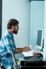 Bearded hipster style adult man working writing on desktop computer in office workspace alone - people and modern job internet connection lifestyle - freelance home sitting male typing on keyboard