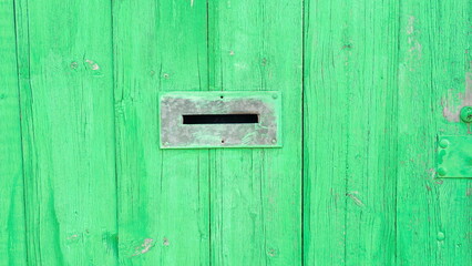 Gap in the fence designed to receive letters. The wooden fence is painted in a vibrant green color