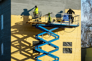 Residential house facade painting works after cladding with wooden planks using scissor lift...