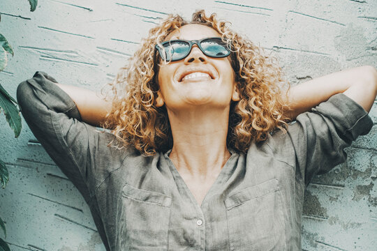 Happy and satisfied woman smiling and looking in the air with green nature ivy on both side. Portrait of joyful female people standing agains an outdoor grey wall. Concept of happiness. One person