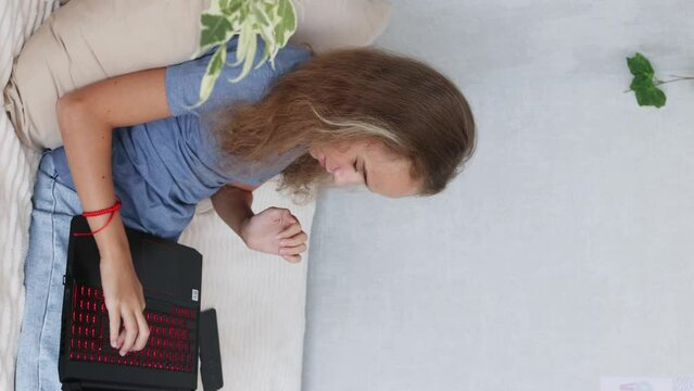 A teenage girl with an open laptop is sitting on her bed typing in her bedroom