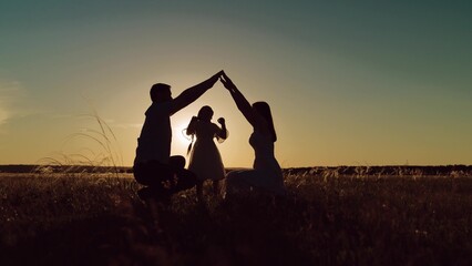 Figures of parents entwine hands above daughter amidst field. Silhouettes of parents holding hands...