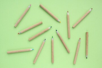 Multi colored pencils isolated on green background. Back to school concept. Sketching and drawing hobby. Stationery supply store. Education process. Top view. Minimal style composition