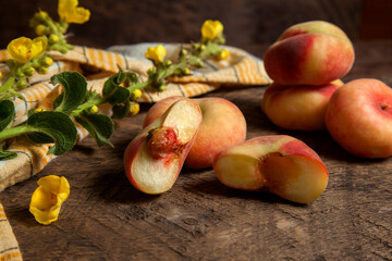Naklejka na ściany i meble Half and several whole saturn peaches or flat peaches on wooden background with yellow kitchen towel..