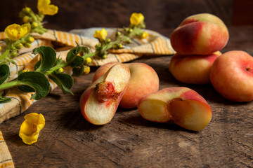Half and several whole saturn peaches or flat peaches on wooden background with yellow kitchen towel..
