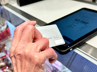 タブレット端末上でクレジットカード決済をする高齢女性の手元