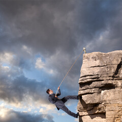 Determined businessman ascends a rugged cliff with the aid of a rope