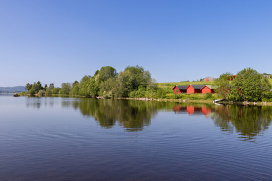 Serene lake Snasavatnet in Steinkjer, Norway, with the wooden Kvam Church peeking through tree branches along the shore