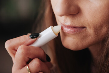Woman using petrolatum on her mouth. Closeup lips background. Applying lip salve on lips with...