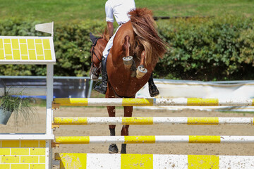Horse from behind jumping over a yellow steep jump, the hooves photographed from behind with focus...