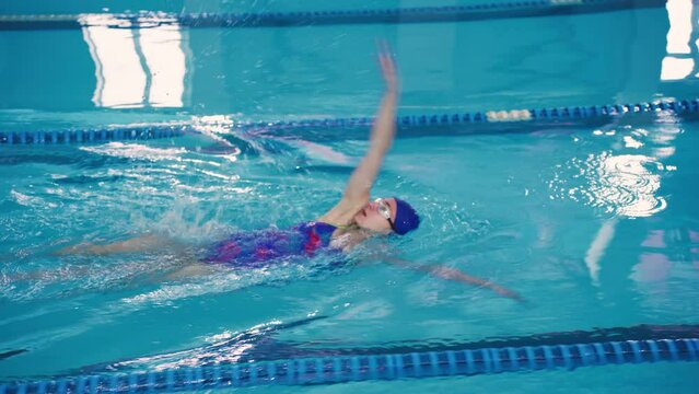 A young woman swimmer in the pool swims using the backstroke technique, Back Crawl. Beautiful attractive girl enjoys swimming.