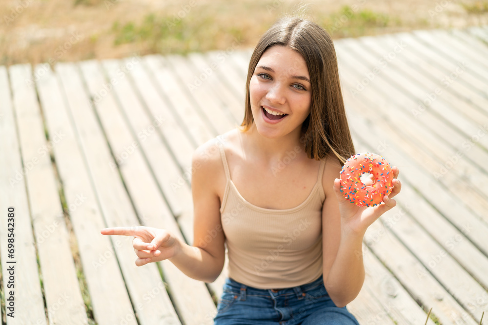 Canvas Prints Teenager girl holding a donut at outdoors surprised and pointing finger to the side